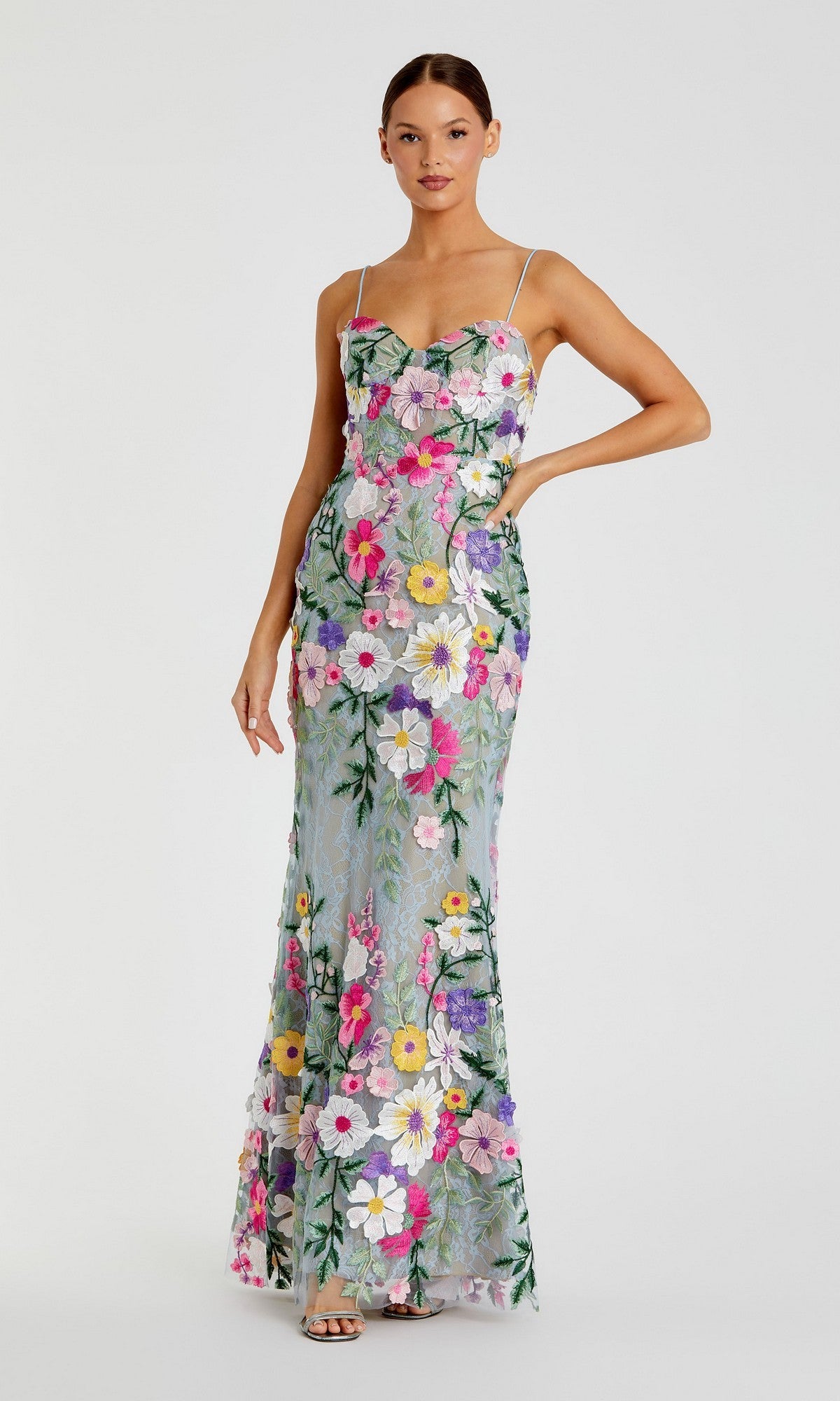 A woman wears the Mac Duggal 68897 Long Formal Dress, a floor-length, sleeveless gown with thin straps and a colorful floral pattern on sheer sage multi fabric.